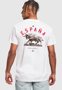 Balta medvilninė marškinėliai su piešiniu, vaizduojančiu bulių ir futbolo kamuolį, viršuje raudonai užrašyta "ESPAÑA" ir "¡A por ellos!".