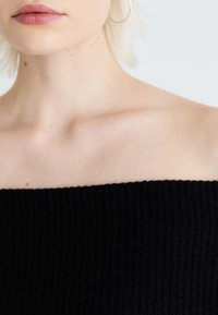 Top nero a coste senza spalline con un tessuto testurizzato, caratterizzato da un scollo dritto e pelle visibile sulle spalle e sulla clavicola.