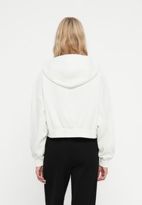 Gekürzter weißer Kapuzenpullover mit gerippten Bündchen und Saum. Weiche Textur, fallende Schultern und lässige Passform. Schlichte Gestaltung, keine sichtbaren Muster.