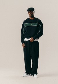 Merineelane kapuutsiga, millel on rohelised ja valged triibud, mustad lõdvad püksid ja valged kingad. Aksessuaaride hulka kuulub must lame müts ja prillid.