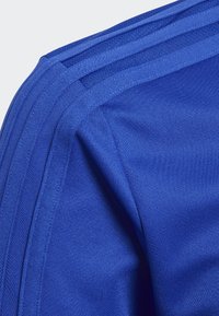 Blaues sportliches Material mit strukturierter Oberfläche, das hervorstechende geschichtete Streifen entlang der Schulter für Designdetails aufweist.