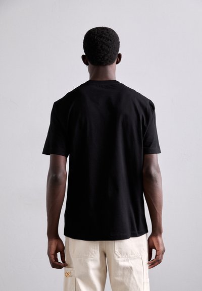 T-shirt en coton noir à manches courtes, col rond et coupe décontractée. Tissu légèrement texturé, vu de dos.