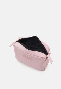 Bolsa de cosméticos rosa hecha de material suave, con una cremallera en la parte superior, diseño redondeado y un forro negro con un detalle de marca sutil.