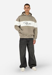 Φούτερ με κουκούλα σε ταοπέ χρώμα με λευκή οριζόντια ρίγα, που διαθέτει μαύρο λογότυπο σε στυλ γραφής. Συνδυάζεται με φαρδιά μαύρα τζιν και λευκά παπούτσια.