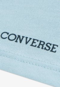 Φυσικό βαμβακερό ύφασμα ανοιχτού γαλάζιου χρώματος με ριγωτή υφή, με την επιγραφή «CONVERSE» σε μαύρο χρώμα κατά μήκος της άκρης, παρουσιάζοντας έναν μινιμαλιστικό σχεδιασμό.