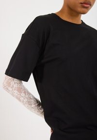Svart kortermet t-skjorte i bomull, kombinert med en gjennomsiktig hvit blonde langermet topp, som viser intrikate blomsterdesign på ermene.