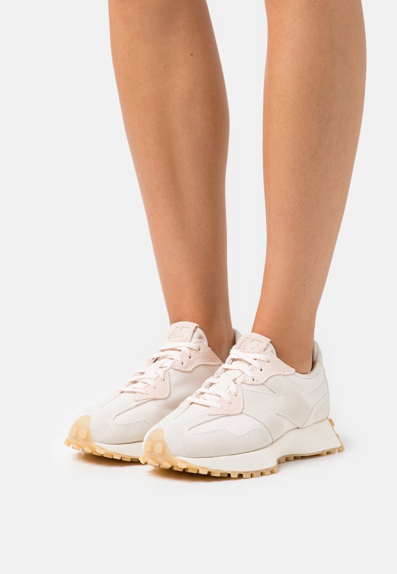 Des chaussures de sport blanches avec un dessus en suède lisse et en mesh, une langue moelleuse, des lacets rose clair et une semelle extérieure en caoutchouc texturé.