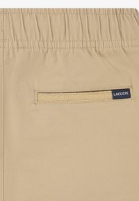 Μπεζ σορτς κατασκευασμένα από ύφασμα με υφή ύφανσης, με πίσω τσέπη που έχει υφαντό διακοσμητικό στοιχείο και μικρή ετικέτα με το λογότυπο της μάρκας.