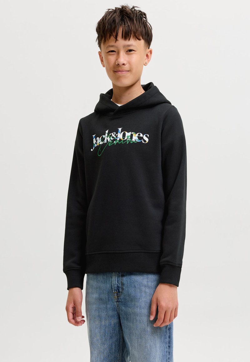 Garçon adolescent portant un sweat à capuche noir Jack & Jones et un jean bleu, debout devant un fond clair uni.