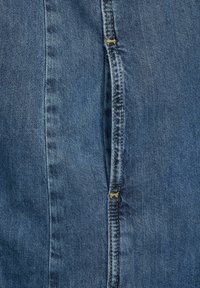 Närbild av blå denimtyg med synlig vertikal söm och dubbelsöm i gul tråd.