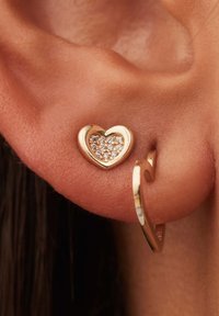 Boucle d'oreille en forme de cœur doré avec des strass étincelants au centre. Fini lisse et poli avec un design en couches subtil.