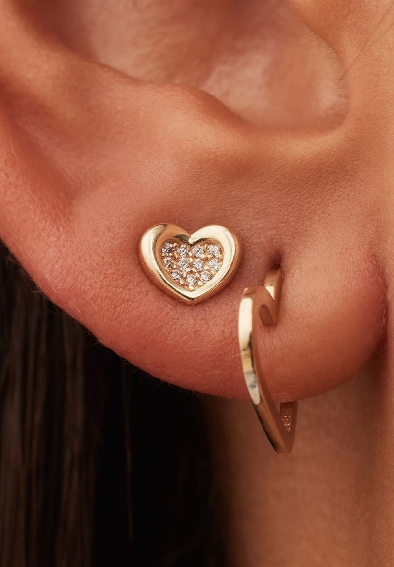 Boucle d'oreille en forme de cœur doré avec des strass étincelants au centre. Fini lisse et poli avec un design en couches subtil.