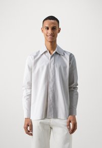 Wit gestreept shirt met lange mouwen, knoopsluiting aan de voorkant, brede kraag en een gestructureerde stof. Gecombineerd met lichtgekleurde broeken.