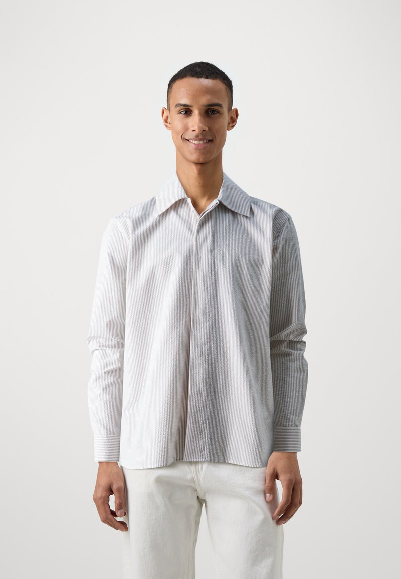 Wit gestreept shirt met lange mouwen, knoopsluiting aan de voorkant, brede kraag en een gestructureerde stof. Gecombineerd met lichtgekleurde broeken.