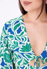 Top con estampado floral en vibrante azul y verde, que presenta un escote en V profundo, espalda con corte y detalle de lazo ajustable. Fabricado en una tela ligera.