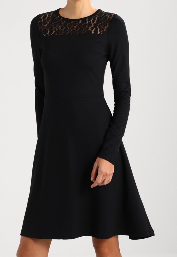 Robe noire à manches longues avec un yoke en dentelle imprimée léopard et une jupe évasée, portée par une personne avec un bras plié sur le côté.