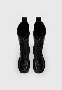 Melnās ādas vidukļa zābaki ar masīvu zoli, detalizētu auklu priekšpusi, sānu rāvējslēdzēju un cilpu uz šahta. Gluda teksturēta apdare.