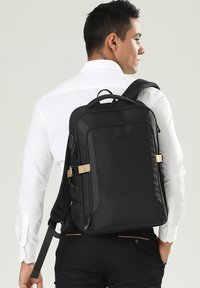 Zaino nero realizzato in tessuto resistente, con un design rettangolare elegante, spallacci regolabili e un accento con fibbia frontale.