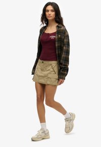 Codzienny strój składający się z ciemnej koszuli w kratę, bordowego topu na ramiączkach, beżowej spódnicy cargo oraz beżowych tenisówek z szarymi akcentami.