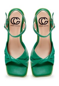 Groene sandalen met hakken, voorzien van een geknoopt ontwerp aan de voorkant, vierkante neus en een verstelbare enkelband. Gemaakt van glad leer met een glanzende afwerking.