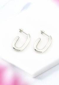 Silver U-formade örhängen med en polerad yta, med en postback för säker användning, visade på en slät vit yta.