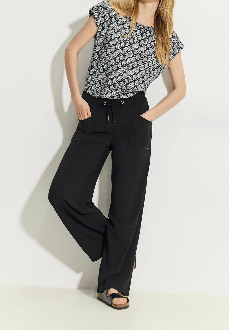 Pantaloni neri a gamba larga con vita elastica e tasche, abbinati a una maglietta a maniche corte con motivo in bianco e nero. Design casual.