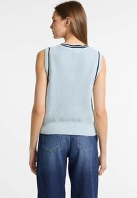 Hellblaues, ärmelloses Strickoberteil mit gerippter Textur. Marinefarbene Akzente am Halsausschnitt. Trägt es mit hochtaillierten dunklen Jeans.