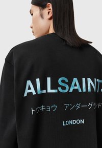 Sweatshirt noir avec un grand texte bleu aqua au dos, portant les mots "ALLSAINTS" et "LONDRES", accompagnés de caractères japonais.