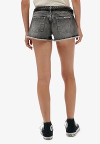 Verbleekte zwarte denimshorts met rafelige zomen, voorzien van achterzakken en een zwarte gevlochten riem. Gecombineerd met zwarte hooglopende sneakers.