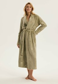 Długi, oliwkowozielony szlafrok wykonany z miękkiego, strukturalnego materiału. Posiada kołnierz szali, pasek do samodzielnego wiązania oraz wzór liści wytłoczony na powierzchni.
