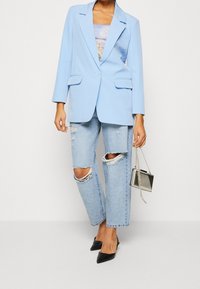 Ljusblå kavaj med skräddarsydd design, framfickor, i kombination med slitna ljusblå jeans, svarta spetsiga klackar och en silverhandväska.