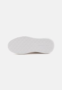 Semelle d'une basket blanche avec une bande de roulement à motif et le nom de la marque "MODI AGRETTE D" embossé près de la zone du talon.