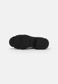 Semelle de chaussure noire avec trois rayures horizontales texturées, bout arrondi et finition lisse. Le matériau semble caoutchouté et flexible.