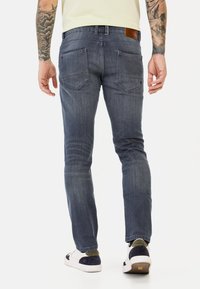 Slanke, donkerblauwe denim jeans met achterzakken, subtiele vervaging en een leren patch op de taille. Gecombineerd met witte en blauwe sneakers.