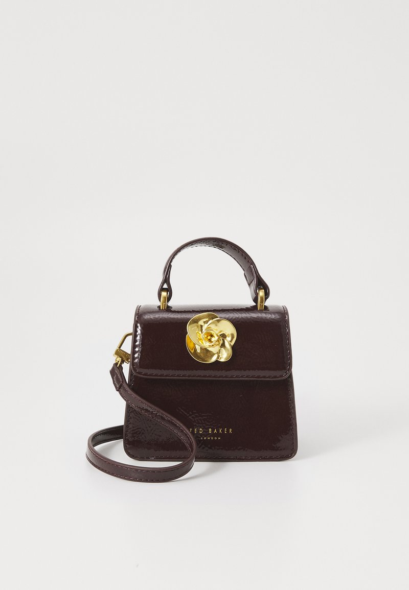 Miniväska i mörk burgundisk patenterad läder med strukturerad design, guldblomaccent, avtagbar rem och präglad logotyp.