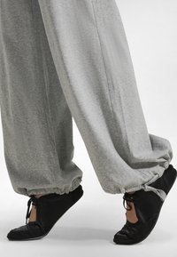 Pantalones deportivos grises de corte ancho en tela suave con puños fruncidos. Zapatos negros bajos con cordones y detalle de punta abierta.