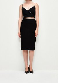 Top corto nero con spalline sottili e design diagonale, abbinato a una gonna a tubo nera al ginocchio e décolleté neri a punta.
