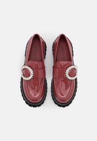 Mocassins en cuir verni bordeaux avec une semelle noire épaisse, présentant une boucle décorative ornée de cristaux sur la sangle.