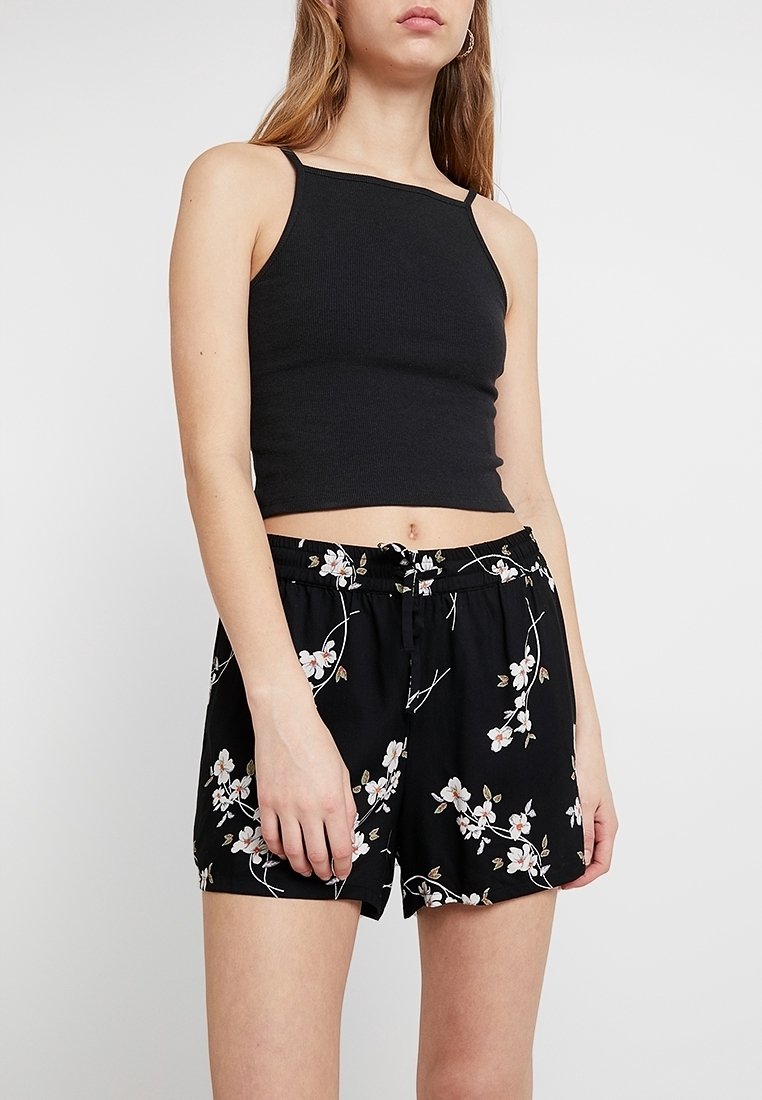 Top corto a coste nero abbinato a pantaloni corti neri con motivo floreale, dotati di cintura con coulisse e tessuto leggero.