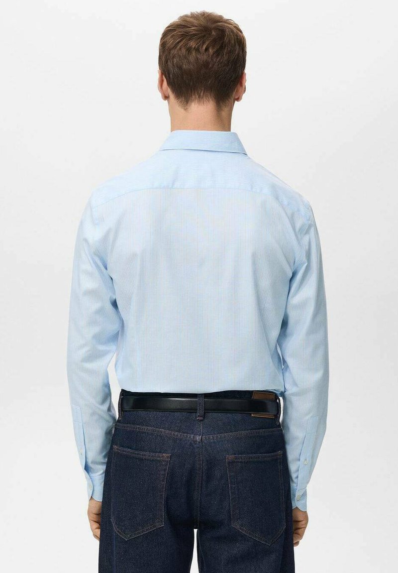 Hellblau gestreifte, langärmelige Bluse mit einem Rückenpasse-Detail, in dunkle Jeans eingesteckt und einem schwarzen Gürtel. Glatte Textur und klassisches Design.