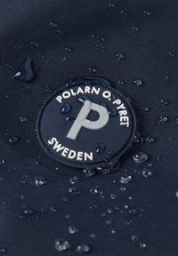 Laine tummansininen kangas, jossa on vesipisaroita, ja jossa on pyöreä logo, jossa on valkoinen "P" ja teksti "POLARN O. PYRET SWEDEN" valkoisilla ja harmailla yksityiskohdilla.