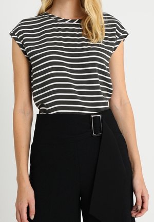 Femme portant un haut sans manches à rayures horizontales noires et blanches, rentré dans un pantalon noir taille haute avec une boucle de ceinture rectangulaire.