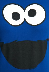 Blue cotton T-shirt featuring a large black and white graphic of wide eyes and a mouth, resembling a cartoon character.