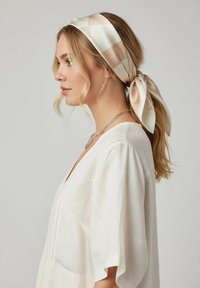 Zijden haarband met een geometrisch patroon in crème en blush. Vastgebonden aan de achterkant, gecombineerd met een losse witte blouse met geborduurde accenten.