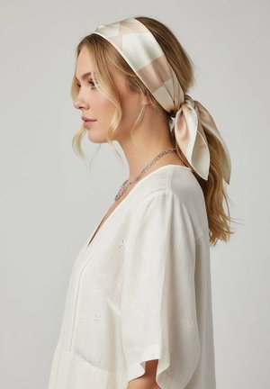 Zijden haarband met een geometrisch patroon in crème en blush. Vastgebonden aan de achterkant, gecombineerd met een losse witte blouse met geborduurde accenten.