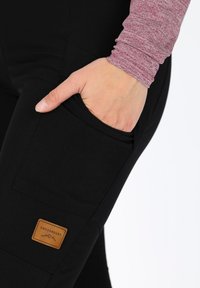 Black stretch pants feature a side pocket and a brown leather tag labeled "Swedemount." The texture is smooth and the design is form-fitting.
