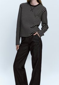 Maglietta a maniche lunghe a righe bianche e nere abbinata a pantaloni larghi scuri, che mostrano una vestibilità comoda e una texture morbida del tessuto.