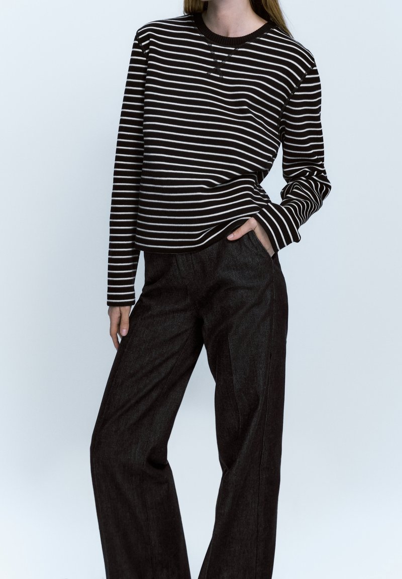 Maglietta a maniche lunghe a righe bianche e nere abbinata a pantaloni larghi scuri, che mostrano una vestibilità comoda e una texture morbida del tessuto.