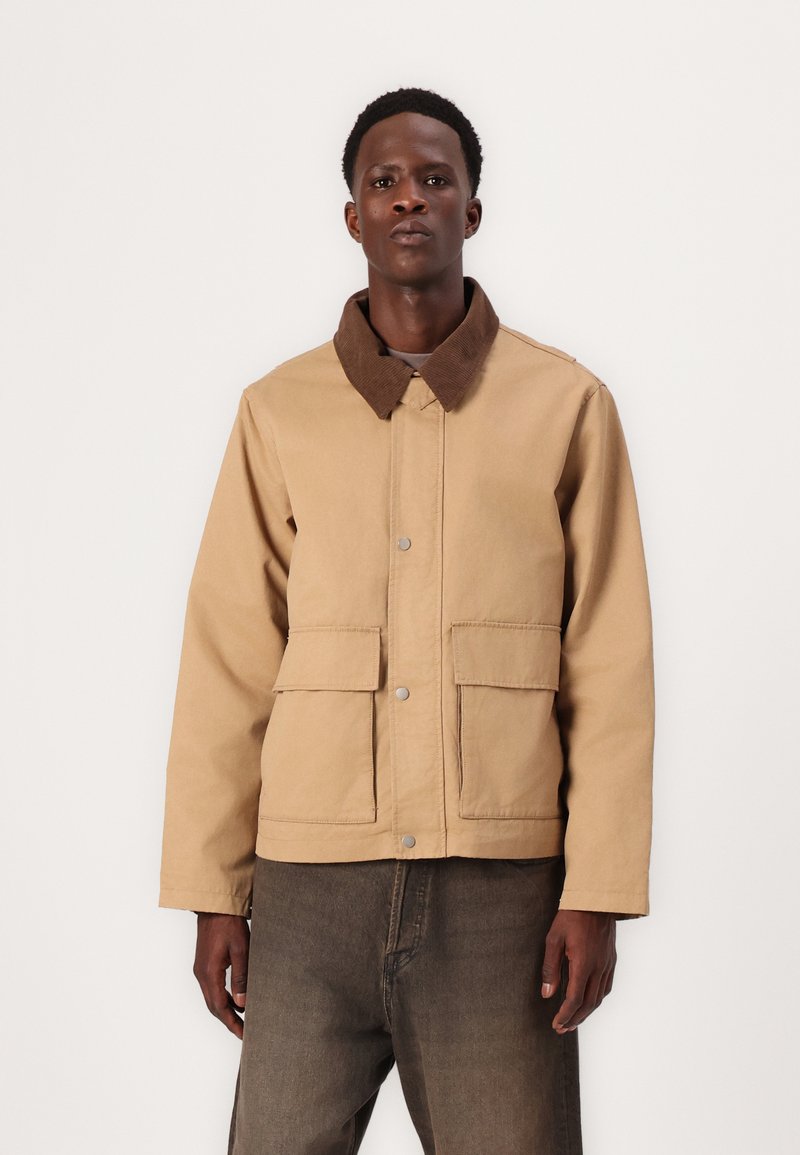Beige jacket with a brown corduroy collar, snap button closure, and two front pockets. Fabric appears sturdy with a smooth texture.