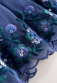Marineblauw tule stof met ingewikkeld bloemrijk borduurwerk in tinten blauw en groen, geaccentueerd met zilveren pailletten en gezoomde randen.